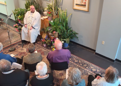 A clergy member preaching, surrounded by flowers and plants