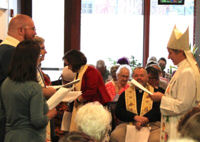 Bishop blessing a seated clergy member amid the congregation