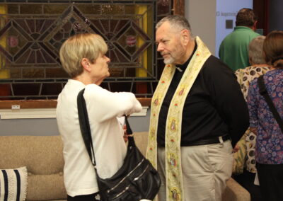 A congregation member and clergy member in conversation near the stained glass
